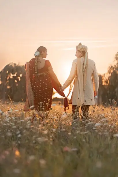 Un couple en tenues indiennes de dos dans un champ au coucher du soleil.