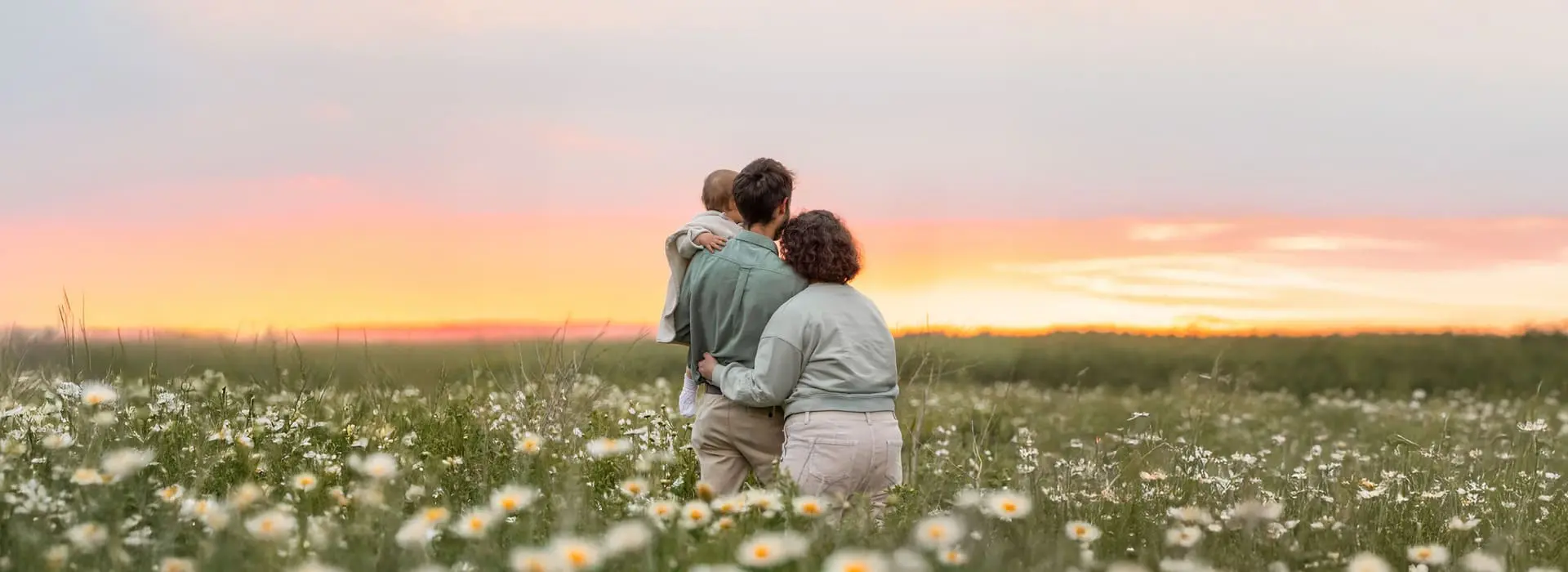 Un couple avec un bébé dans un champ au coucher du soleil.