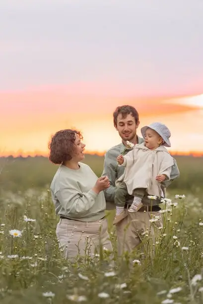 Un couple avec leur bébé dans un champ au coucher du soleil.
