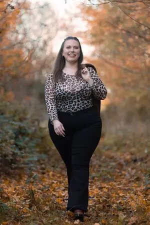 Femme élégante en pantalon noir et haut léopard dans une forêt.