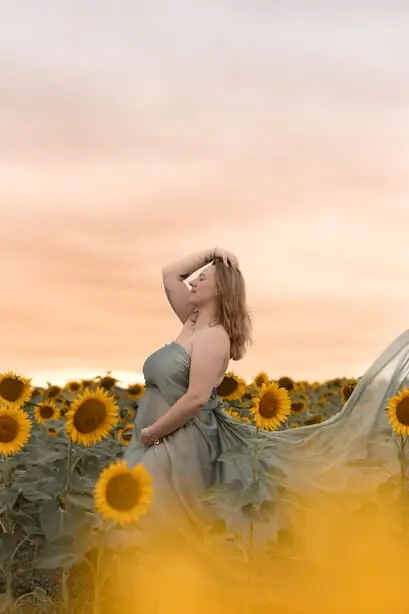 Femme enceinte dans un champ de tournesols au coucher du soleil. Tons verts et jaunes.