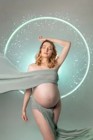 Femme enceinte en séance photo grossesse stylisée avec décor lumineux et voilage. Tons verts.