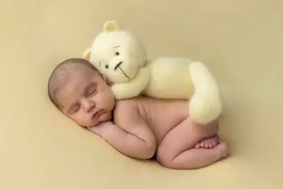 Bébé couché sur le ventre en posing avec un ourson en peluche jaune sur le dos.