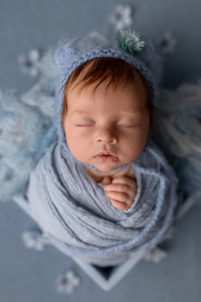 Bébé emmailloté avec bonnet tricoté. Dans les tons gris-bleus.