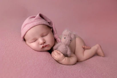 Bébé avec un bonnet et un ourson dans les bras dans les tons roses