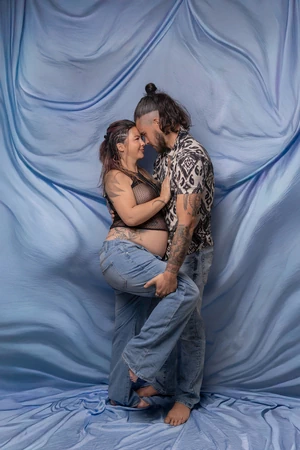 Couple de profil en face à face, lors d’une séance photo grossesse avec fond bleu.