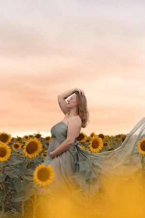 Femme enceinte avec voilage vert à l'extérieur dans un champ de tournesols.