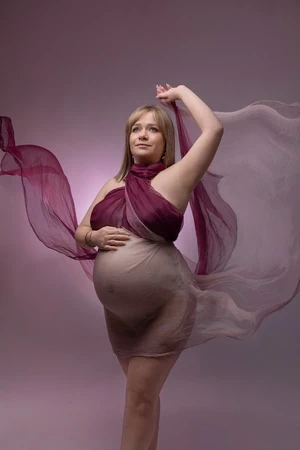Femme enceinte en séance photo grossesse stylisée avec voilage. Tons bordeaux.