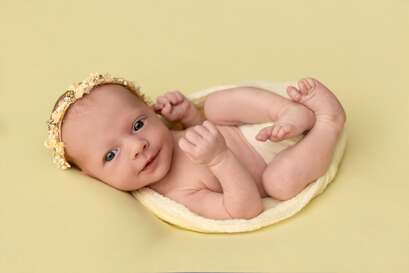 Bébé couché sur le dos avec une couronne de fleurs sur la tête, mains et pieds repliés. Tons jaunes