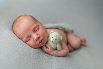 Bébé en posing couché sur le ventre avec une peluche dans les bras, dans des tons verts.